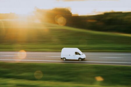 A white minibus travelling along a country road at sunset